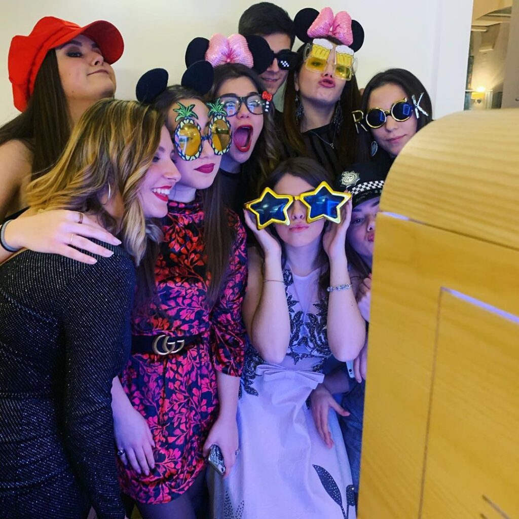 Ragazze con occhiali da sole buffi in posa insieme alla festeggiata davanti a un photo booth compleanno